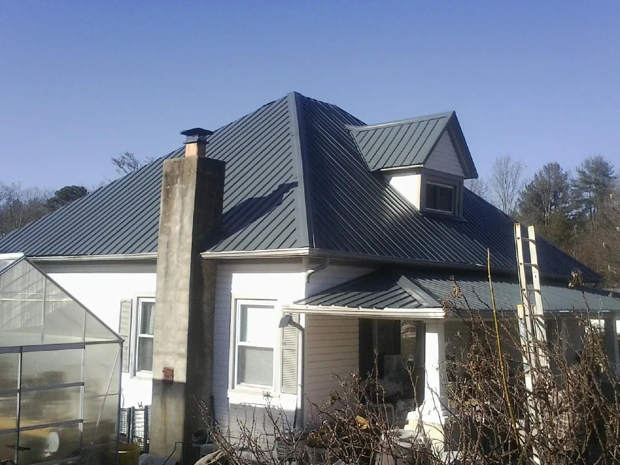 Dark blue standing seam metal roof on a white farmhouse with dormer — Slate & Tile Roof Repair by Roofing Brothers in Clayton
