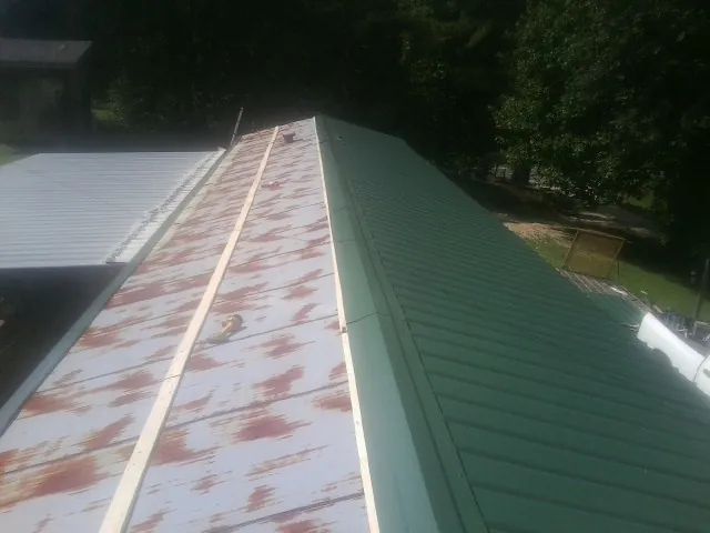 Old rusted panels beside newly installed green metal roofing — Wind Damage Roof Repair by Roofing Brothers in Clayton
